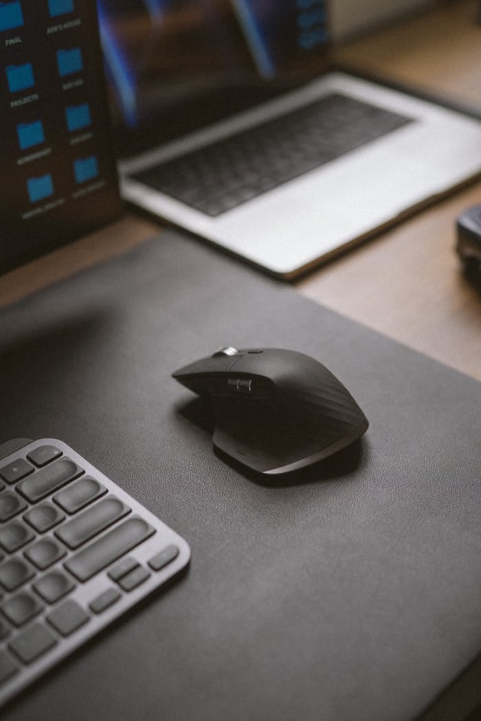 A sleek setup featuring a black wireless mouse, laptop, and keyboard on a desk.