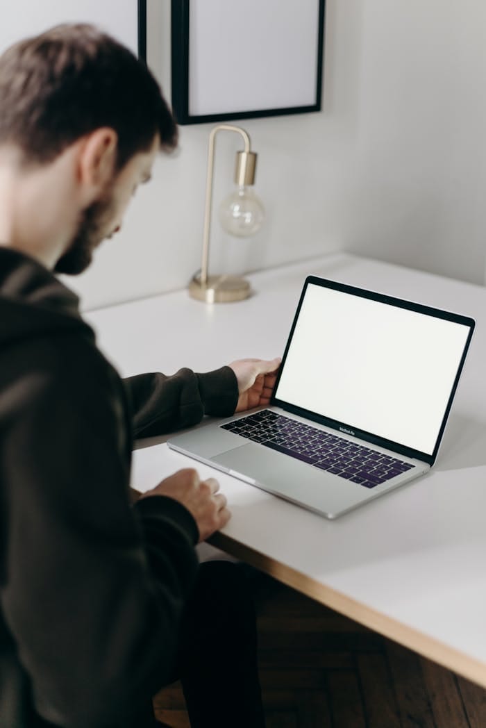 The Art of Drawing Readers In: Your attractive post title goes here Adult man in hoodie using laptop at home with blank screen. Minimalist home office setting.