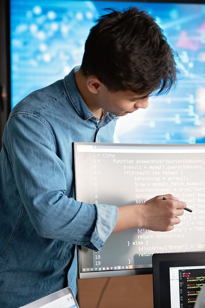 Crafting Captivating Headlines: Your awesome post title goes here Asian male programmer writing code on a computer monitor in an office setting.