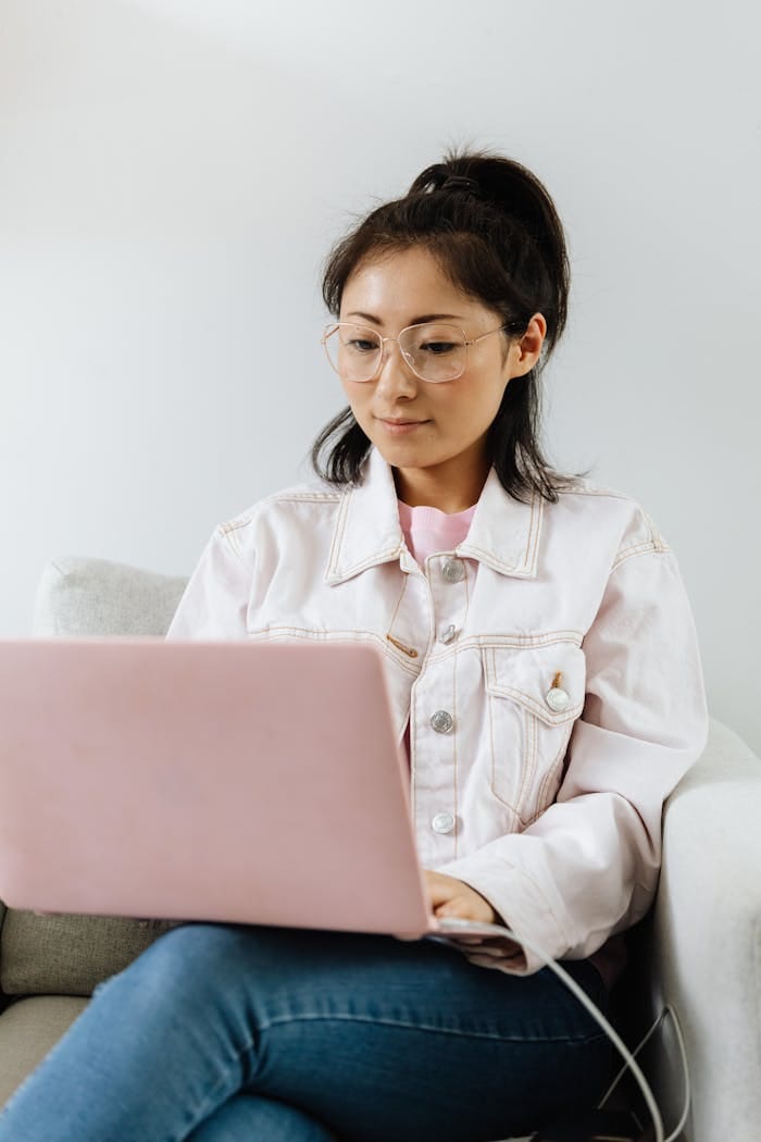 Mastering the First Impression: Your intriguing post title goes here Asian woman with eyeglasses sitting on a couch, focused on her laptop.